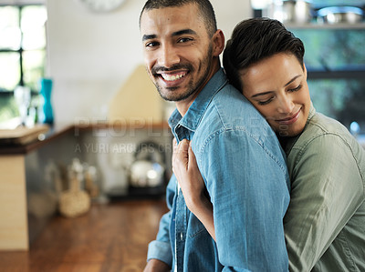 Buy stock photo Shot of a young woman embracing her husband from behind while standing in their kitchen