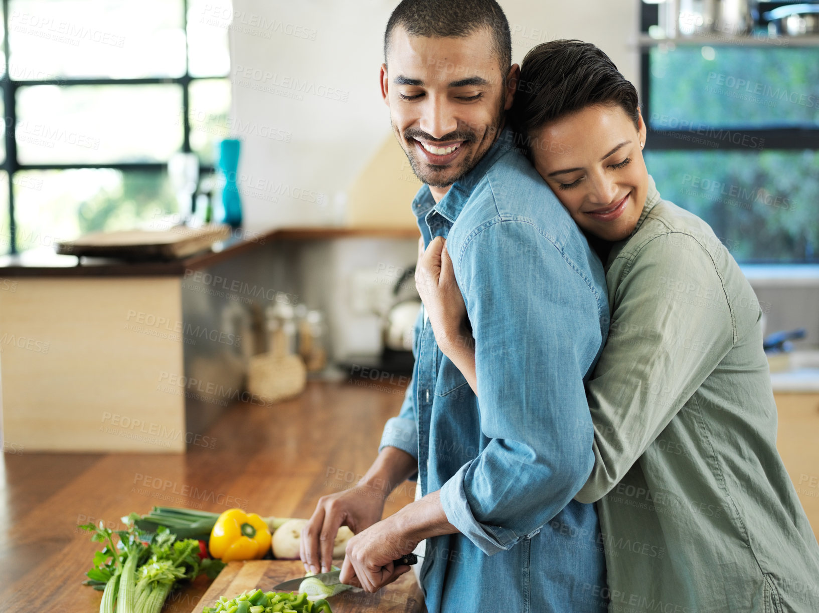 Buy stock photo Shot of an affectionate young couple preparing a meal together in their kitchen