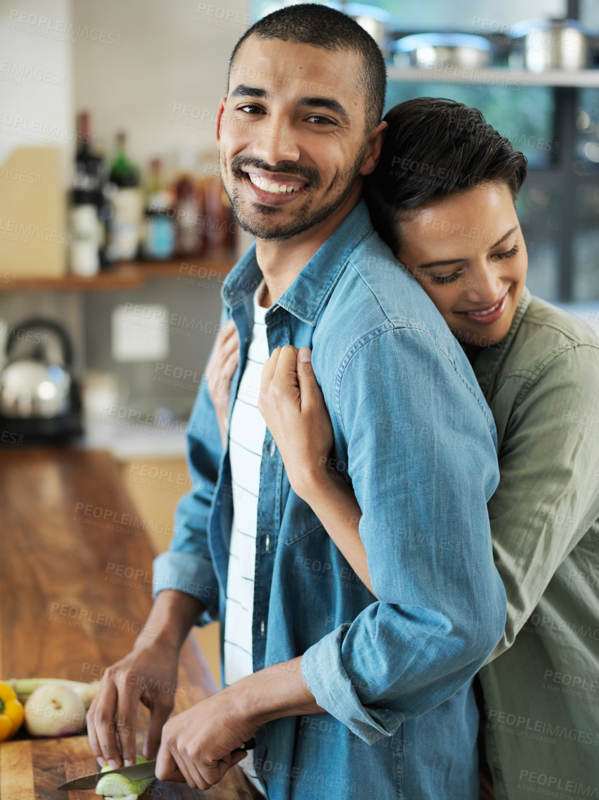 Buy stock photo Portrait of an affectionate young couple preparing a meal together in their kitchen