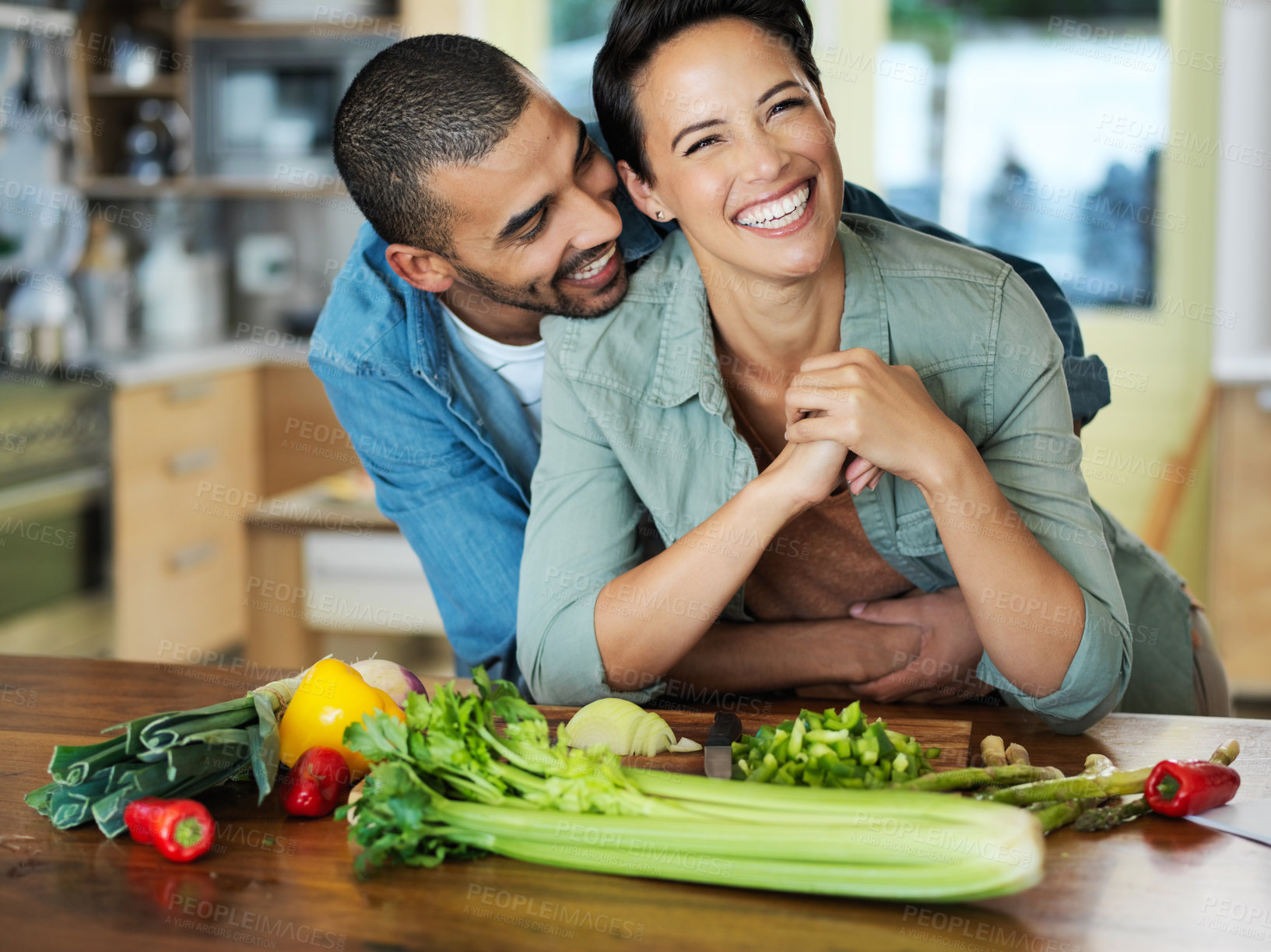 Buy stock photo Portrait of an affectionate young couple preparing a meal together in their kitchen