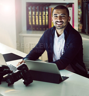 Buy stock photo Portrait of a smiling young photographer working on a digital tablet and laptop in his home office in the early evening