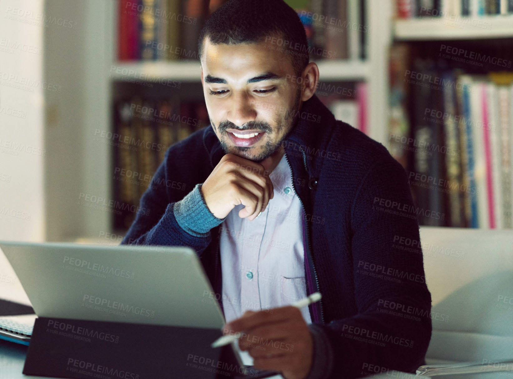 Buy stock photo Shot of a smiling young man working on a digital tablet in his home office in the early evening