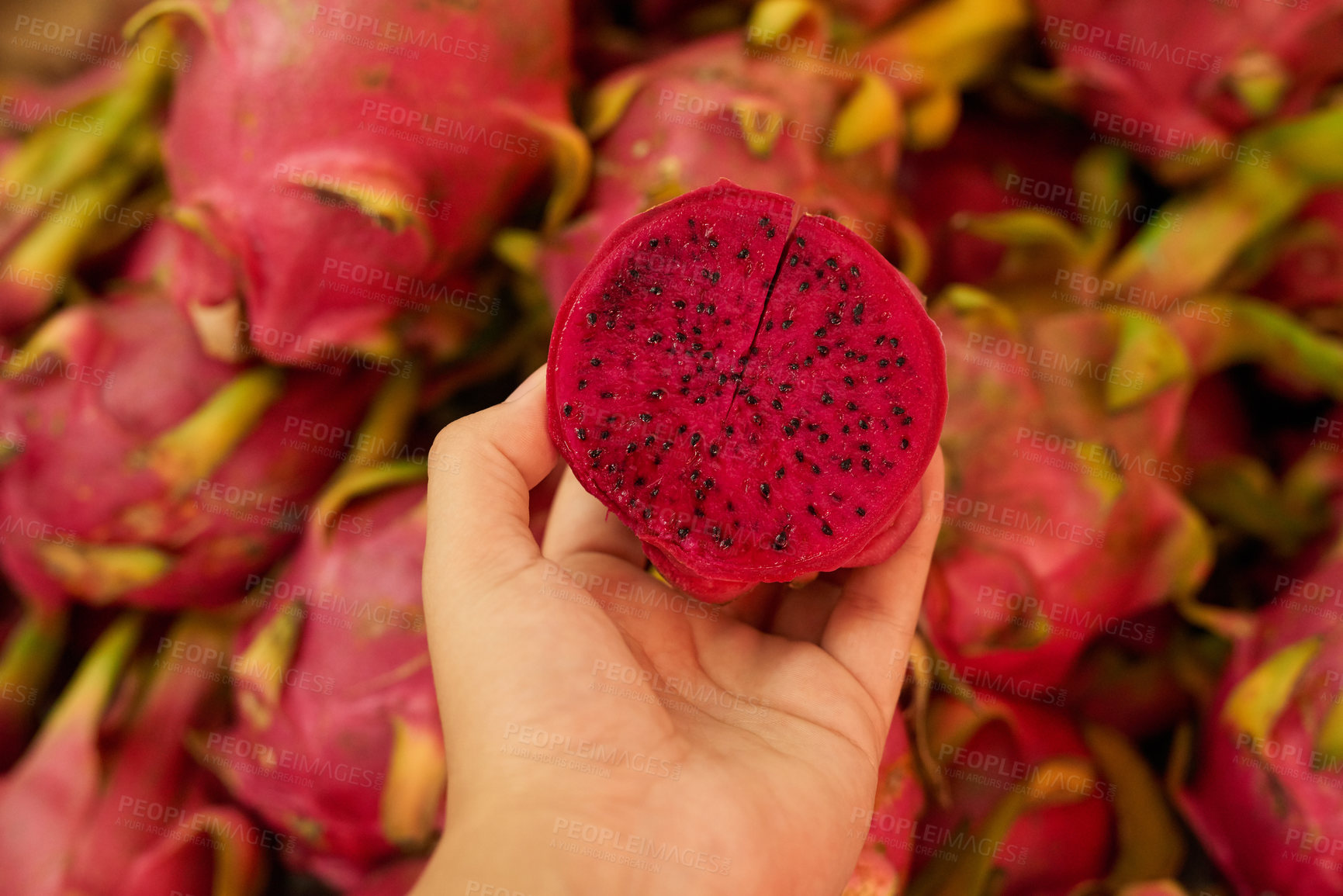 Buy stock photo Shot of an unidentifiable woman holding a halved dragon fruit at a fruit market