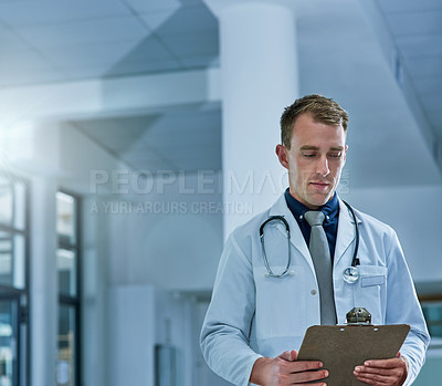 Buy stock photo Shot of a young doctor reading the contents of a patient’s file