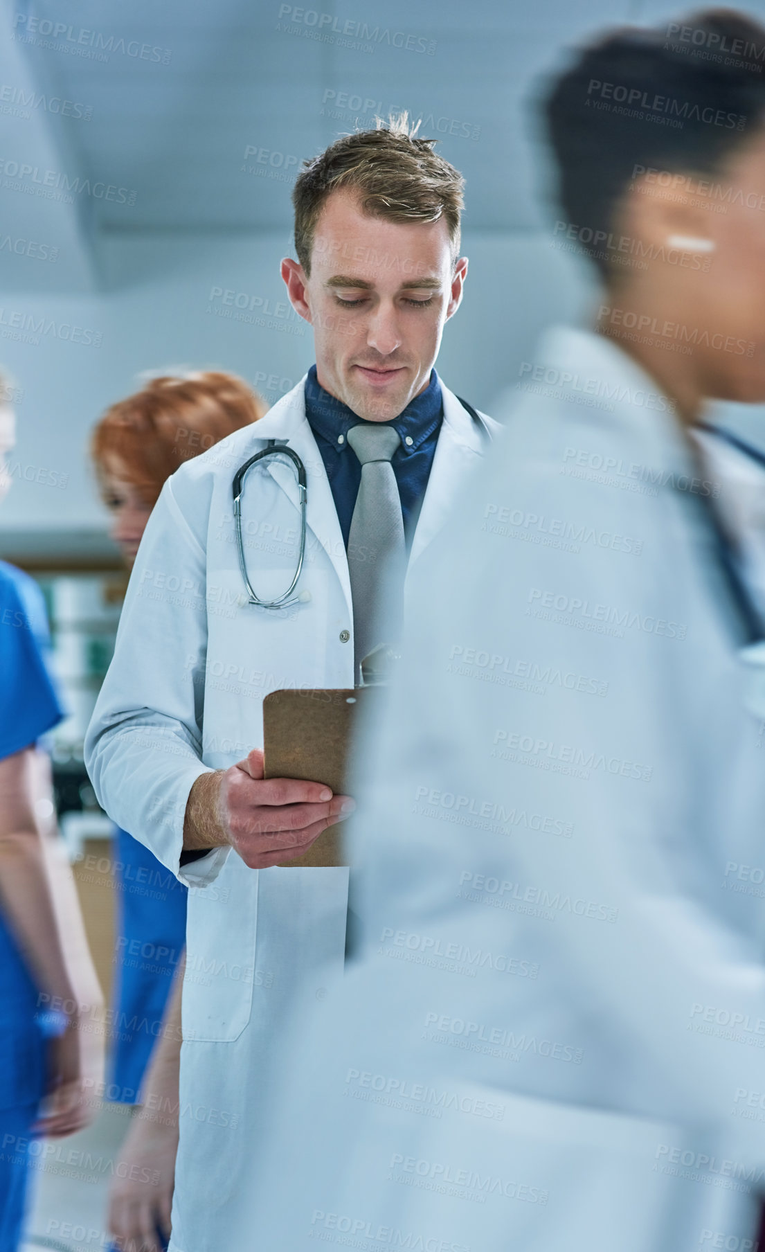 Buy stock photo Shot of a young doctor reading the contents of a patient’s file in a busy hospital
