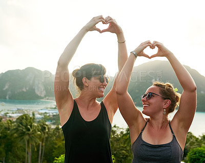Buy stock photo Shot of two friends making a heart shape with their hands while on holiday in Thailand