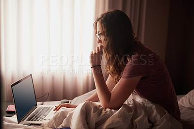 Buy stock photo Shot of a young woman using a laptop while sitting in bed