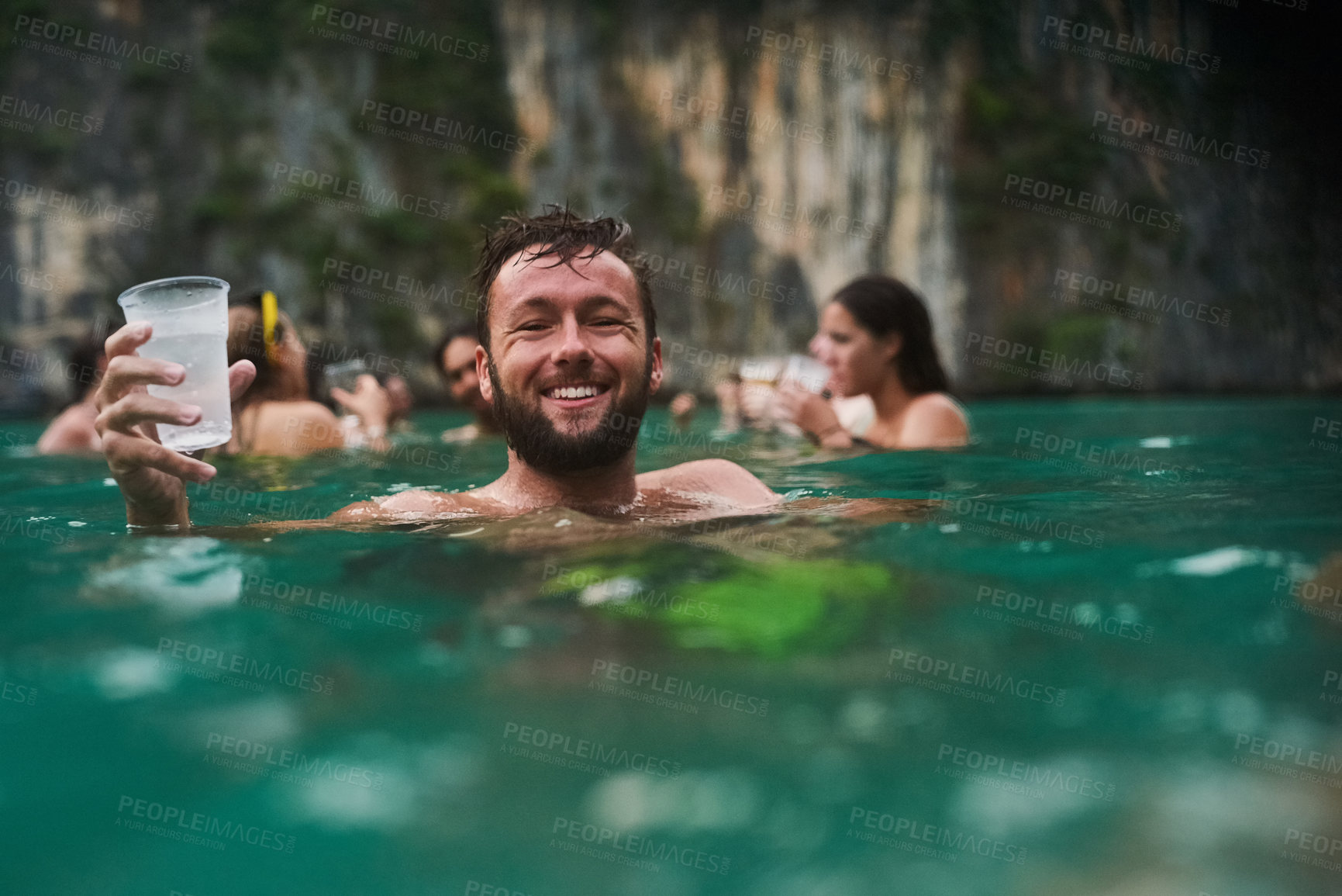 Buy stock photo Portrait of a happy young man enjoying a drink while relaxing in the ocean with his friends