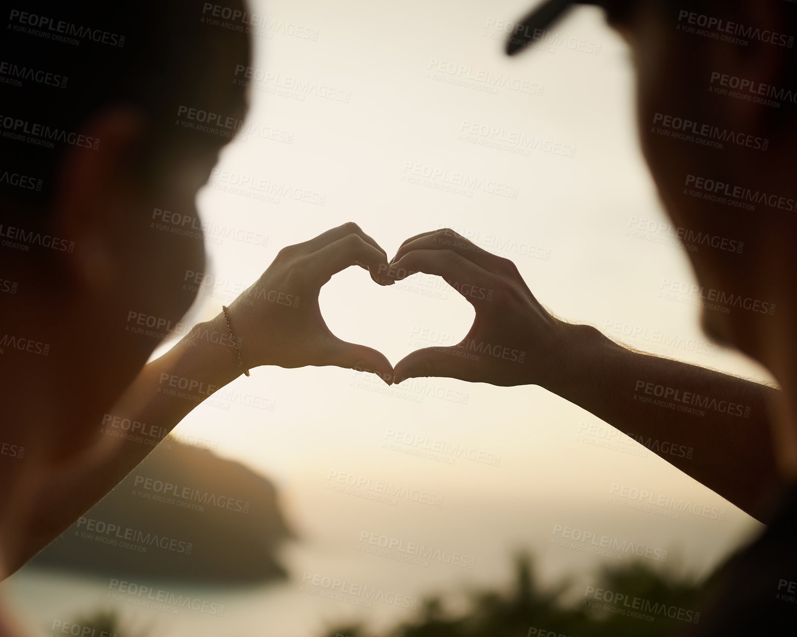 Buy stock photo Rearview shot of a couple making a heart shape with their hands over a sunset landscape