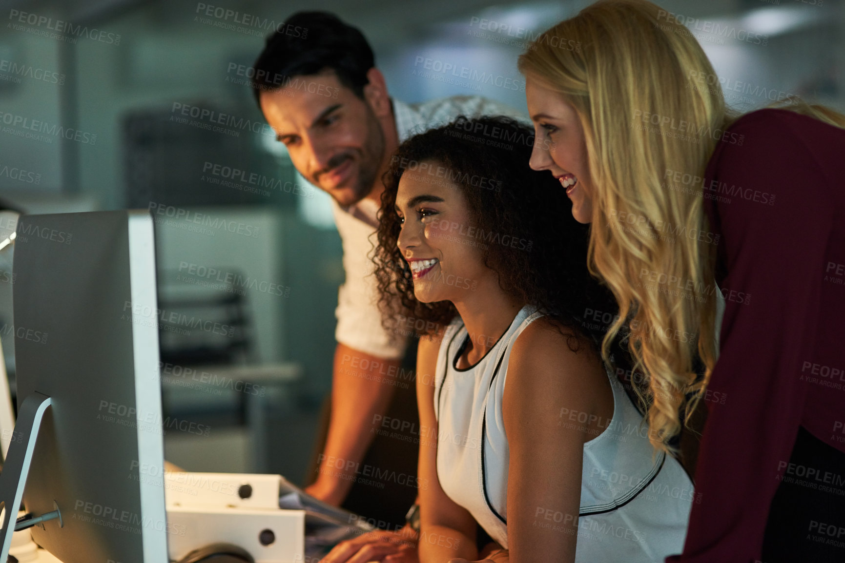 Buy stock photo Shot of a group of young colleagues using a computer together during a late night at work