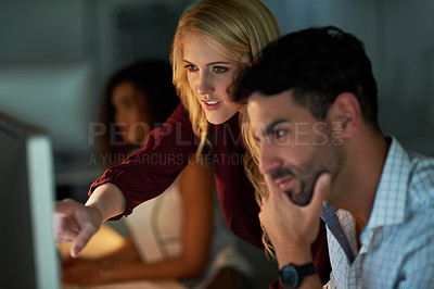 Buy stock photo Shot of two young coworkers using a computer together during a late night at work