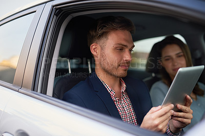 Buy stock photo Shot of a young man looking at a tablet while traveling in a car with his wife