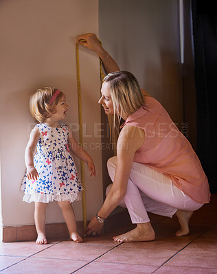 Buy stock photo Shot of a mother measuring her little girl's height at home