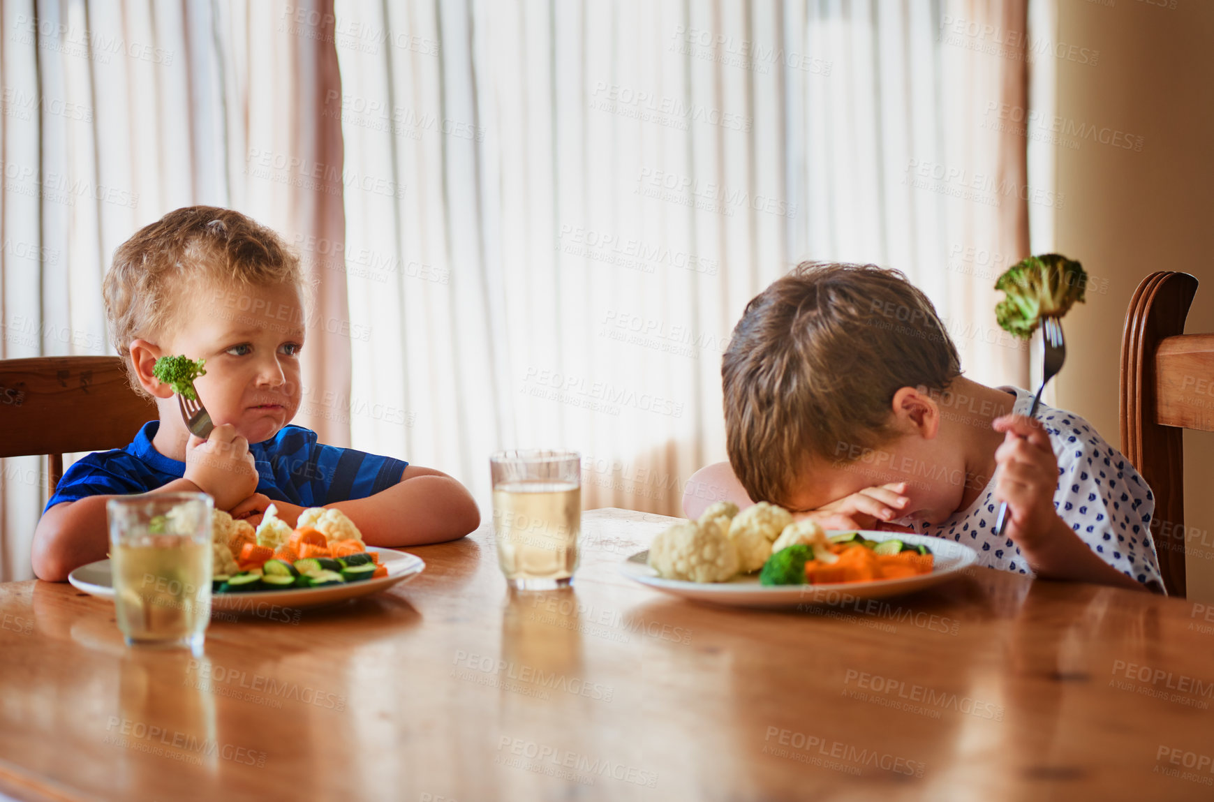 Buy stock photo Shot of two unhappy little boys refusing to eat their vegetables at the dinner table