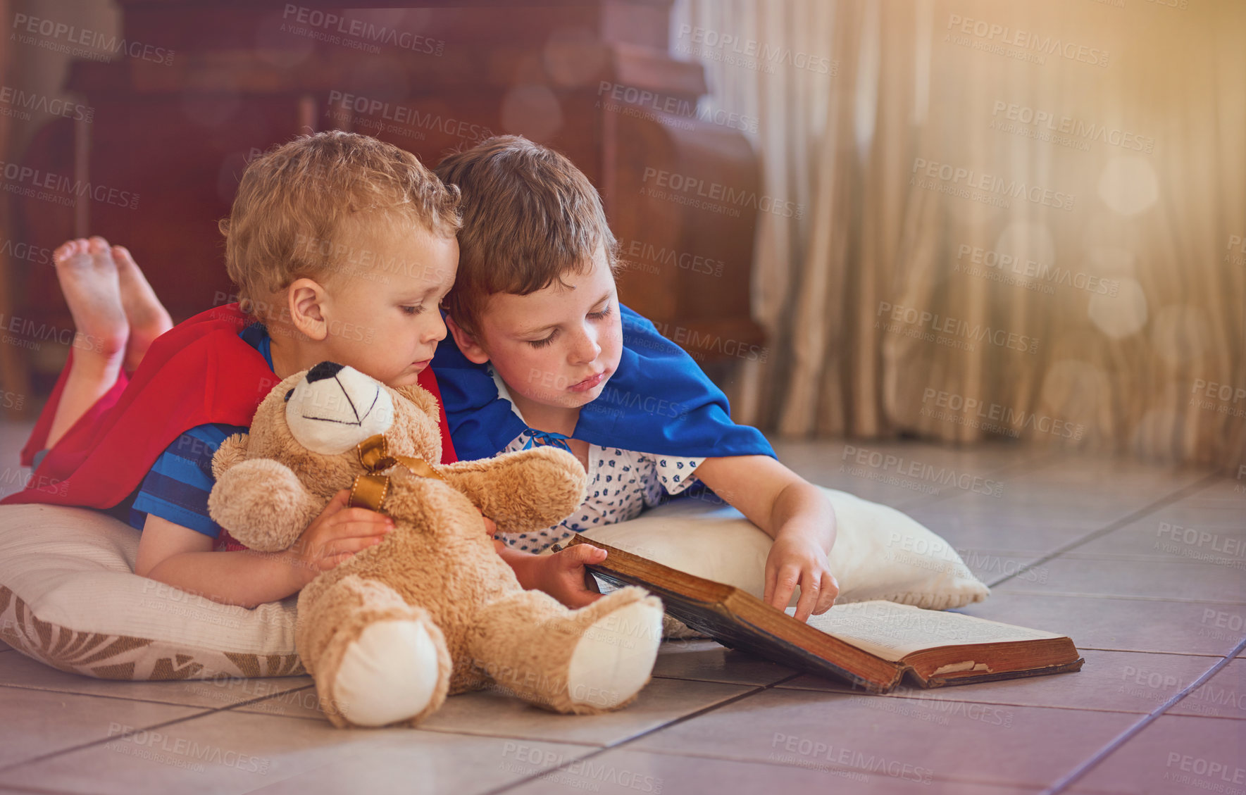 Buy stock photo Shot of two little boys playing with a book while lying on the floor at home