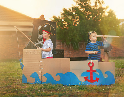 Buy stock photo Shot of a cute little boy and his brother playing pirates outside on a boat made of cardboard boxes