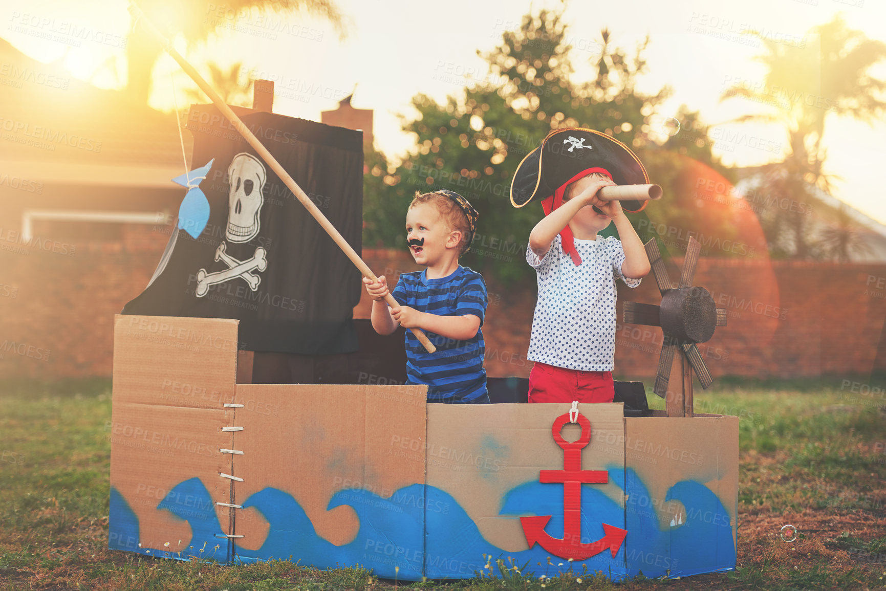 Buy stock photo Shot of a cute little boy and his brother playing pirates outside on a boat made of cardboard boxes