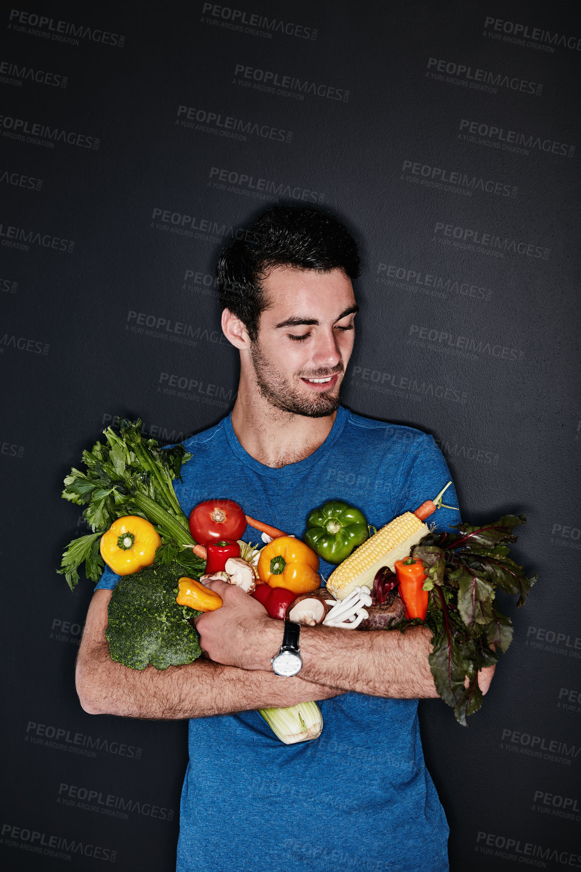 Buy stock photo Studio shot of a young man carrying an armful of healthy vegetables against a dark background