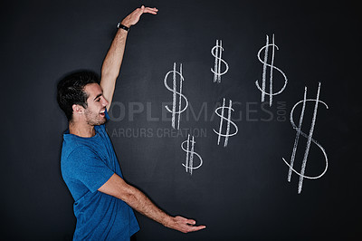 Buy stock photo Studio shot of a young man gesturing over an illustration of a dollars against a dark background