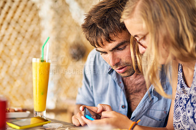 Buy stock photo Shot of a young couple looking at a cellphone together while relaxing in a restaurant