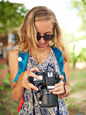 Buy stock photo Shot of a happy young woman looking at photographs on her camera while on vacation