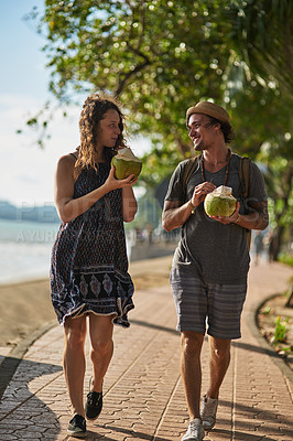 Buy stock photo Shot of a young couple drinking cocktails while walking along the beach