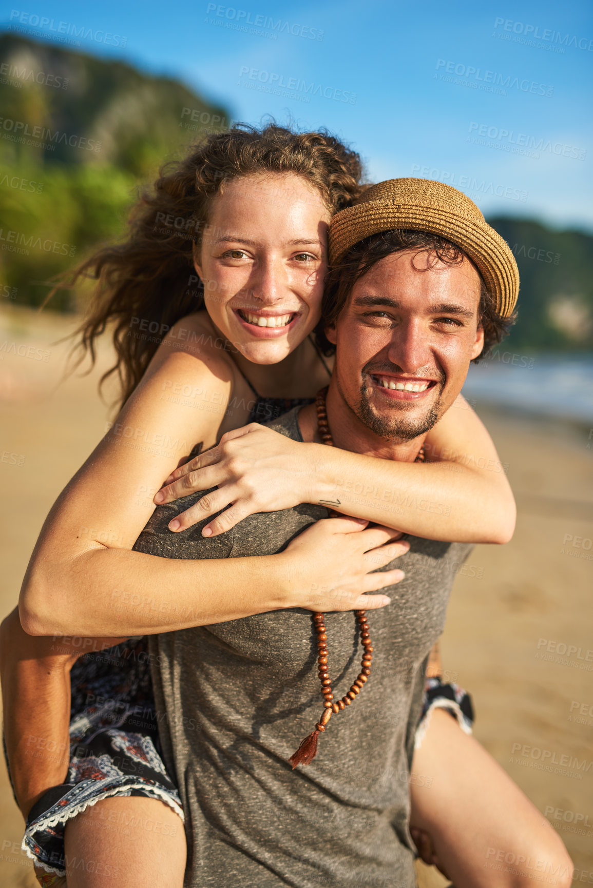 Buy stock photo Portrait of a happy young man giving his girlfriend a piggyback ride on the beach