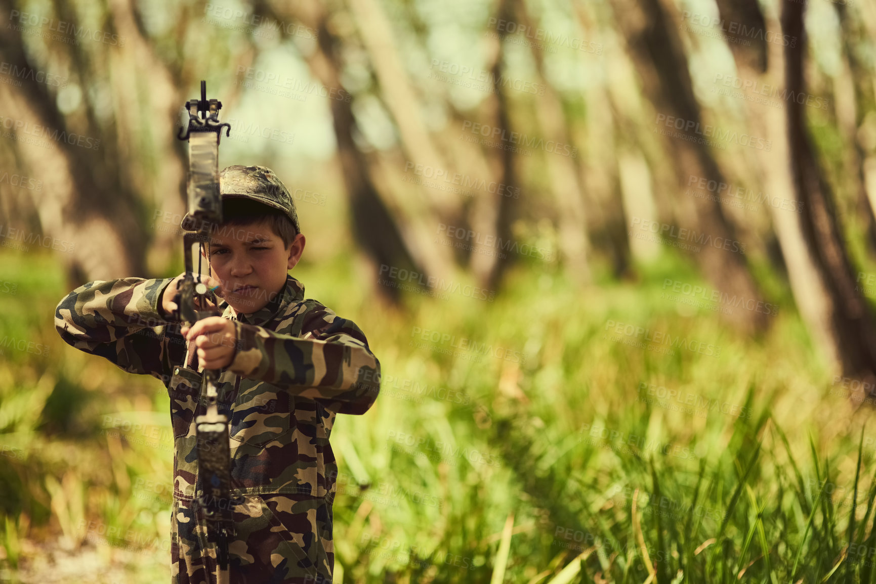 Buy stock photo Portrait of a cute little boy in camouflage playing with his bow and arrow in the woods