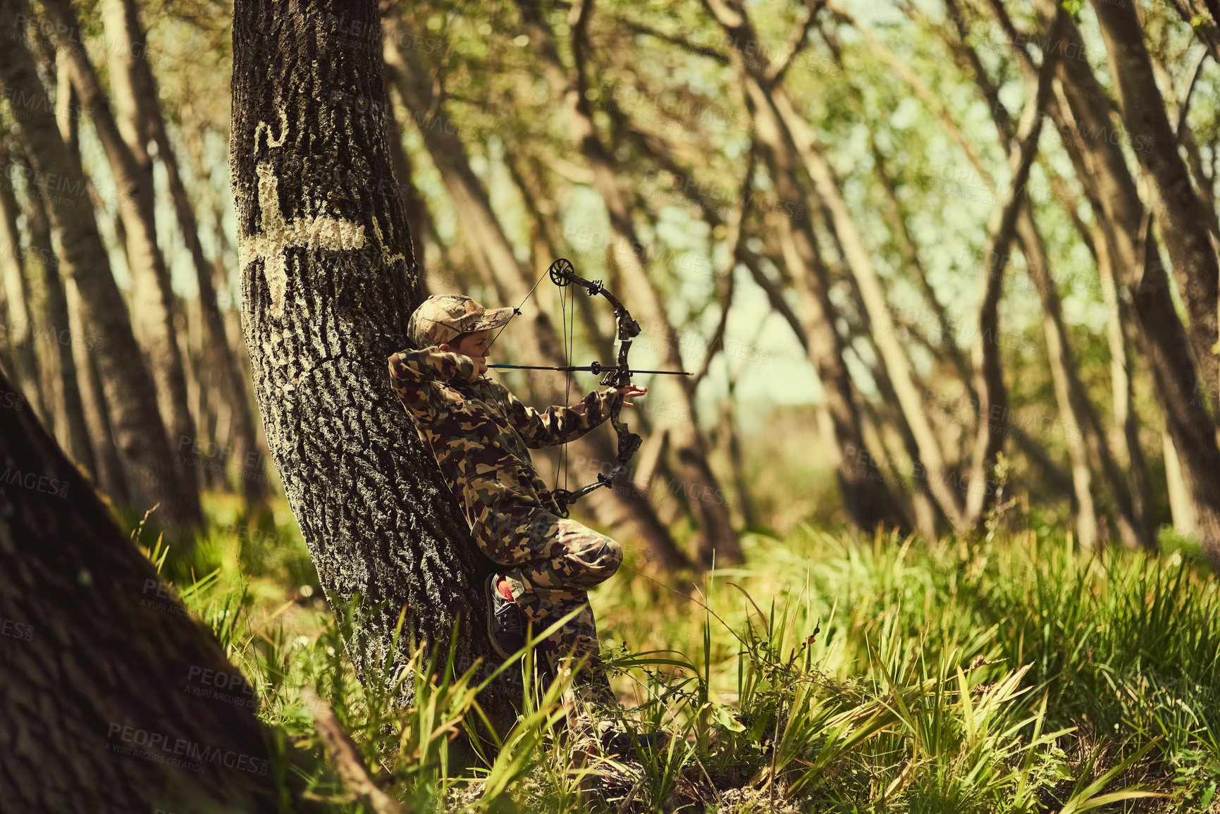 Buy stock photo Shot of a cute little boy in camouflage playing with his bow and arrow in the woods