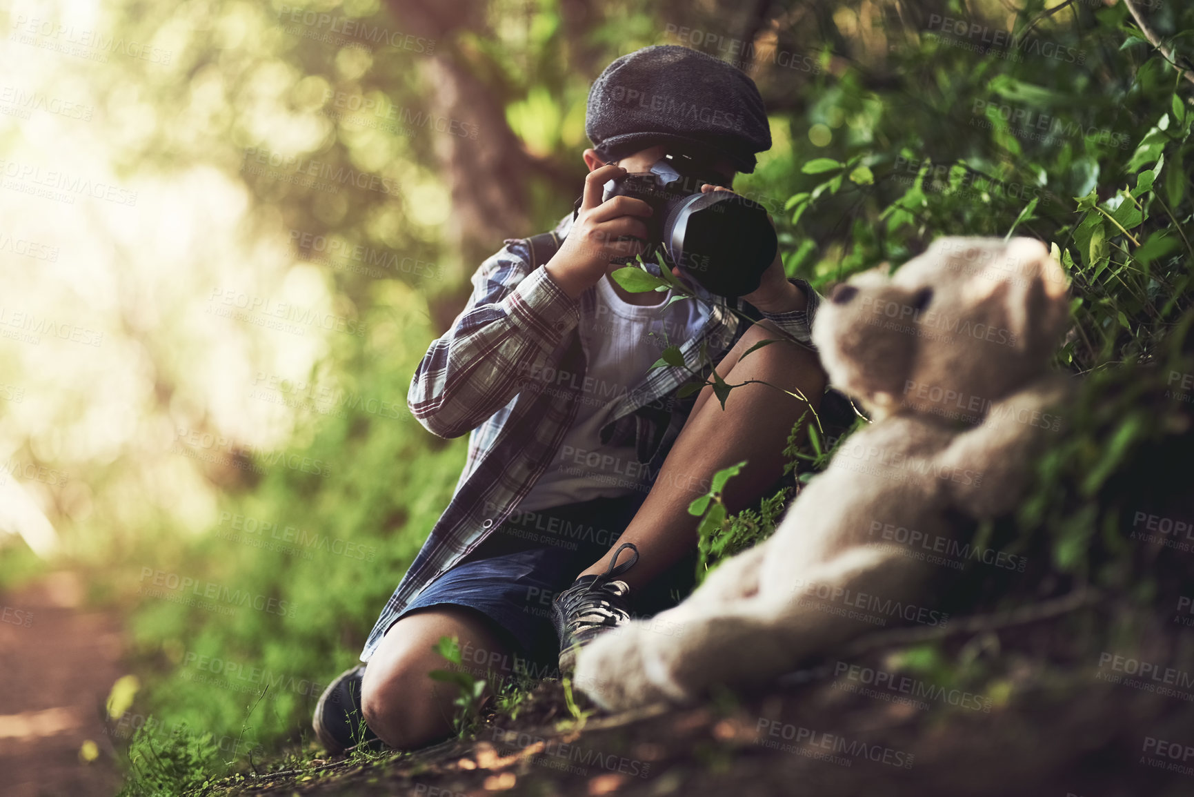 Buy stock photo Shot of an unidentifiable young boy using a camera to take photos of his teddy in the woods