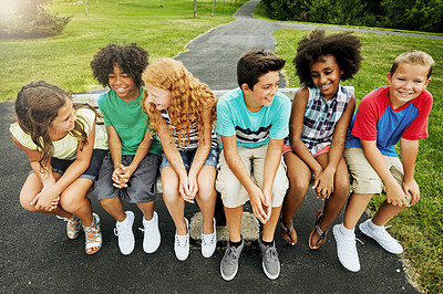 Buy stock photo Shot of a group of diverse and happy kids sitting together on a bench outside