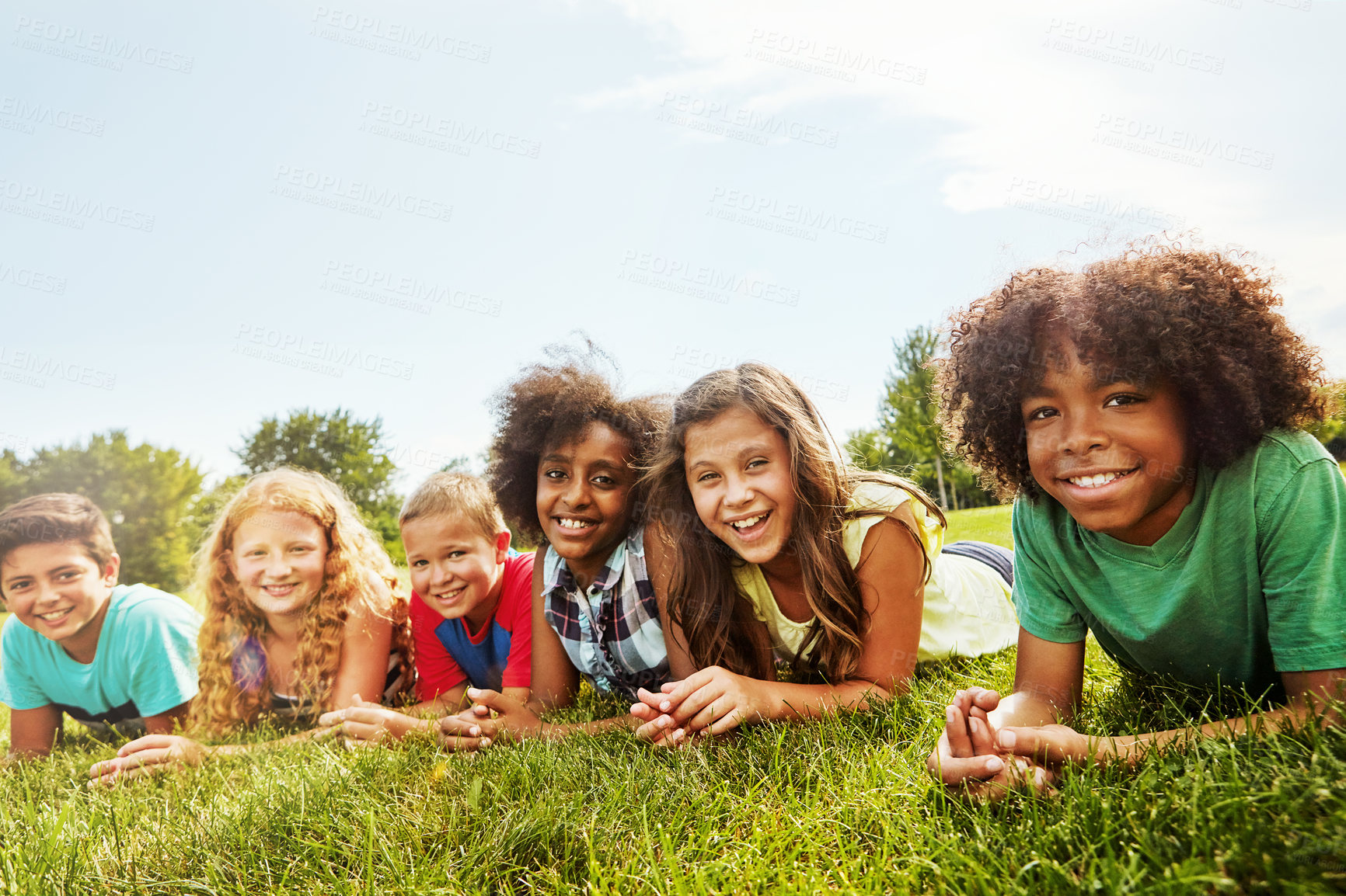 Buy stock photo Portrait of a group of diverse and happy kids lying together on the grass outside