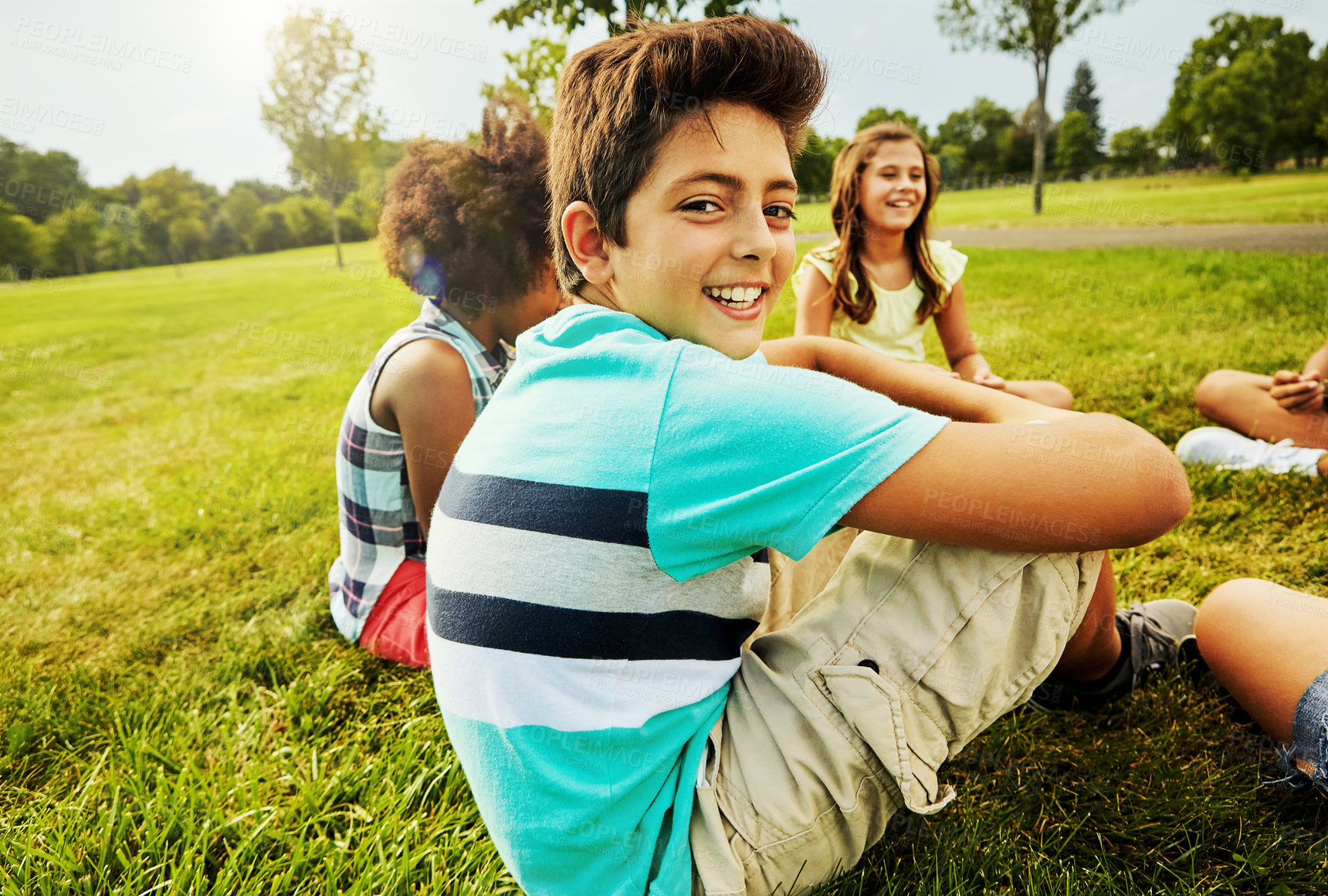 Buy stock photo Portrait of a young boy sitting together with his friends on the grass outside