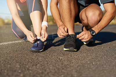 Buy stock photo Cropped shot of two unrecognizable young people tying their laces before a run