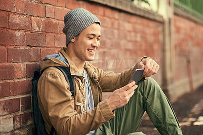 Buy stock photo Cropped shot of a young man texting on his cellphone while out in the city