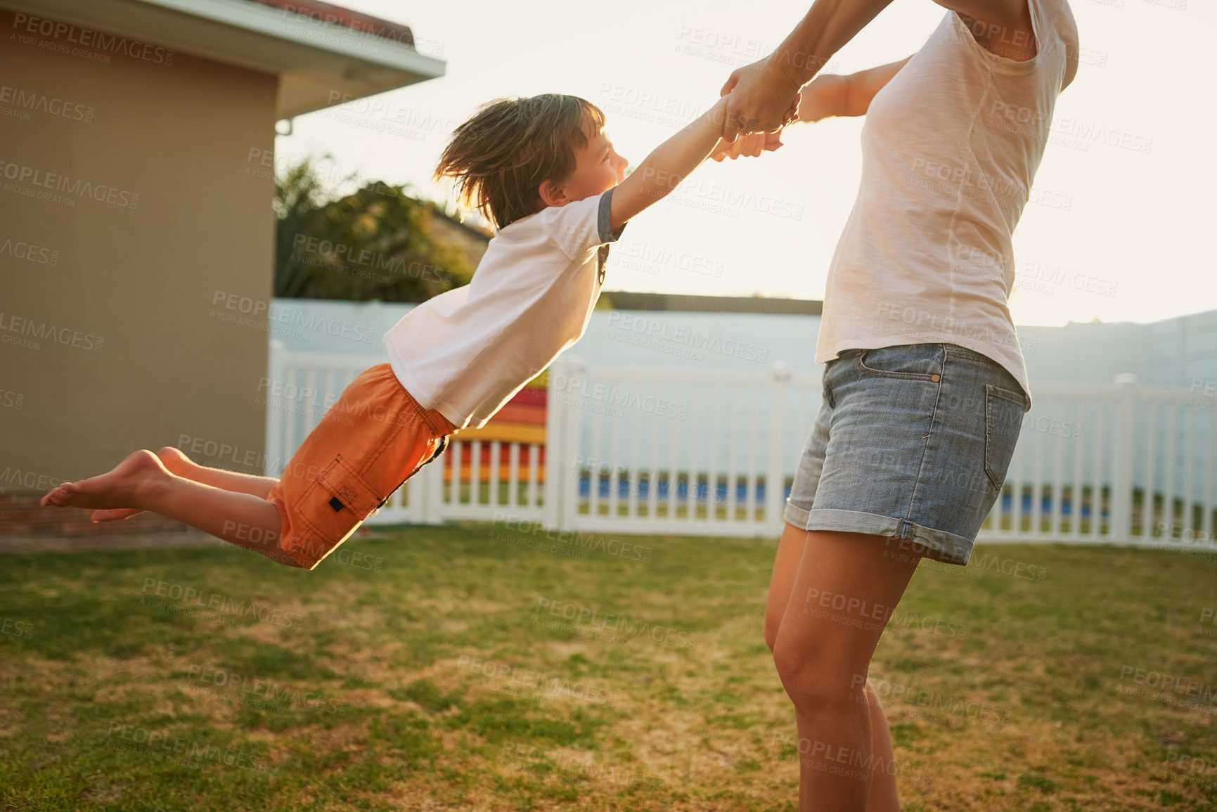 Buy stock photo Shot of a mother playfully swinging her son around in their backyard