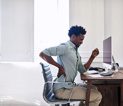 Buy stock photo Cropped shot of a young designer suffering from back pain while working at his desk in an office