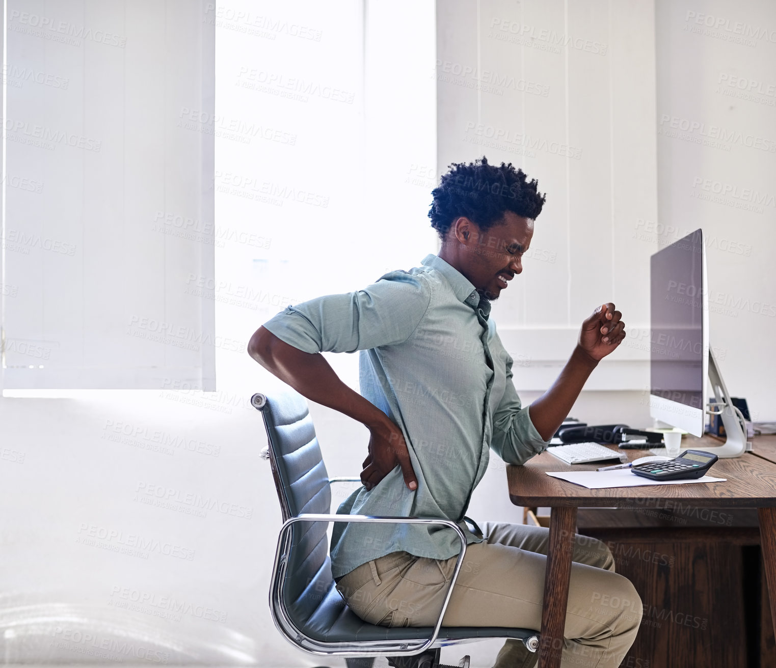 Buy stock photo Cropped shot of a young designer suffering from back pain while working at his desk in an office