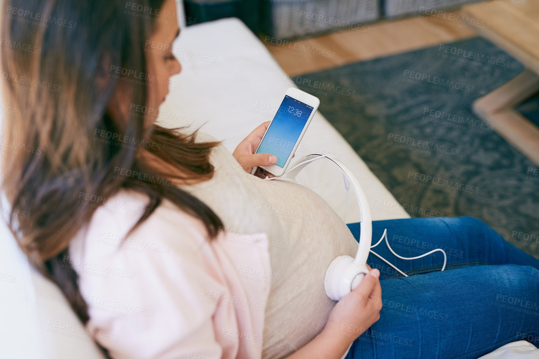 Buy stock photo Relax, phone and pregnant woman on sofa with headphones on stomach for child development in home. Pregnancy, growth and mom on couch with smartphone, sound and music streaming for bonding with baby