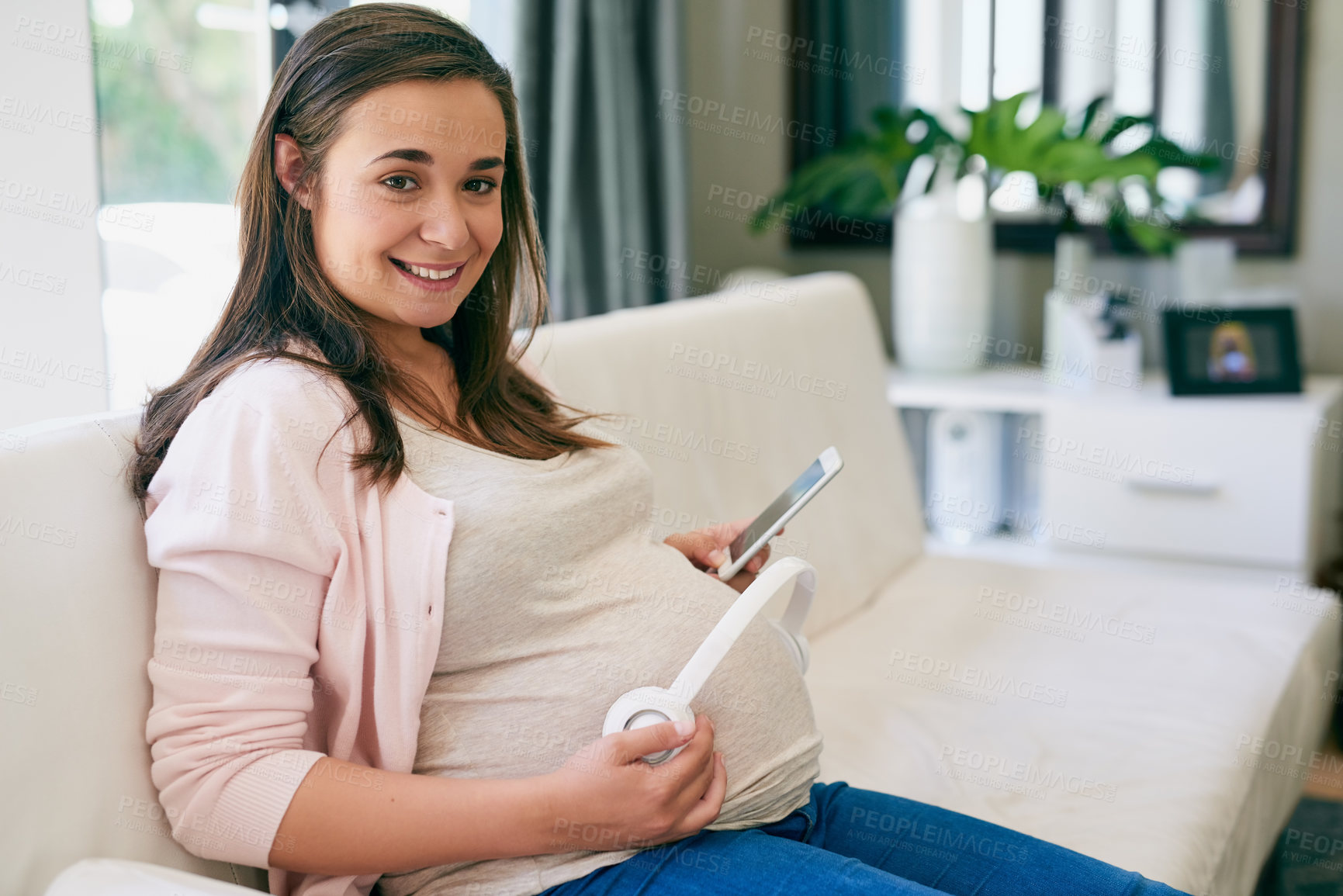 Buy stock photo Portrait, phone and pregnant woman on sofa with headphones on stomach for child development in home. Pregnancy, growth and mom on couch with smartphone, sound and app for music streaming in apartment