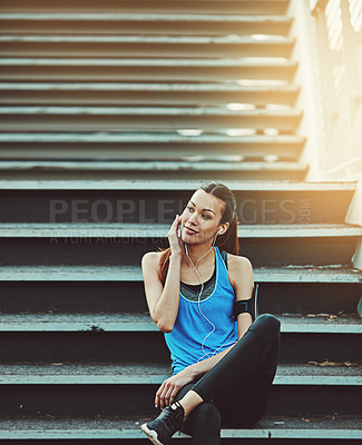 Buy stock photo Shot of a sporty young woman listening to music while sitting on a staircase