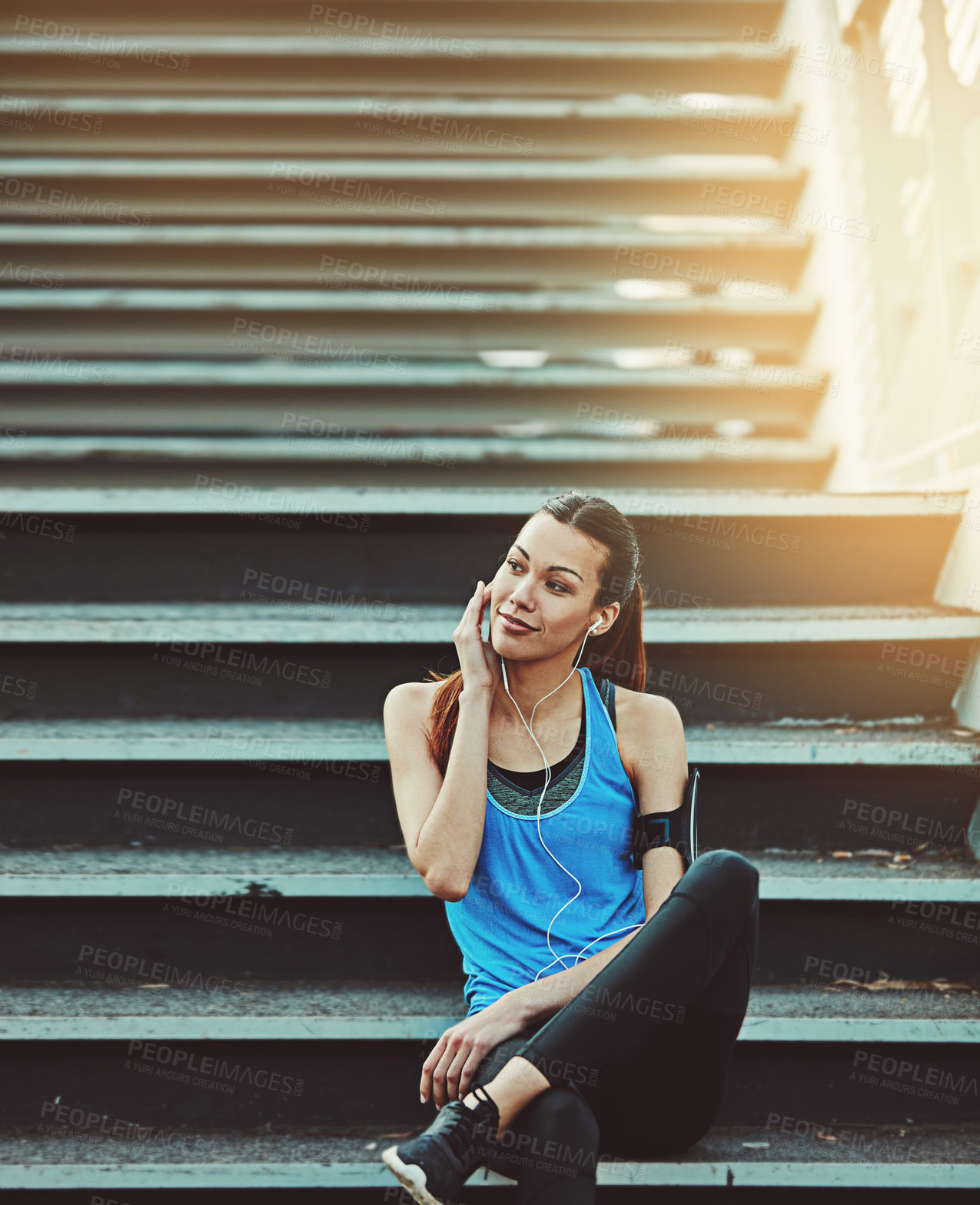 Buy stock photo Shot of a sporty young woman listening to music while sitting on a staircase