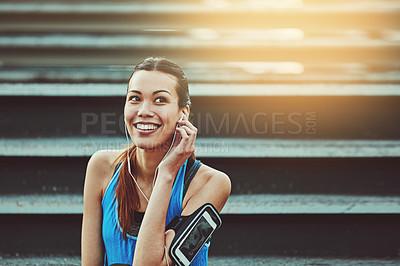 Buy stock photo Shot of a sporty young woman listening to music while sitting on a staircase