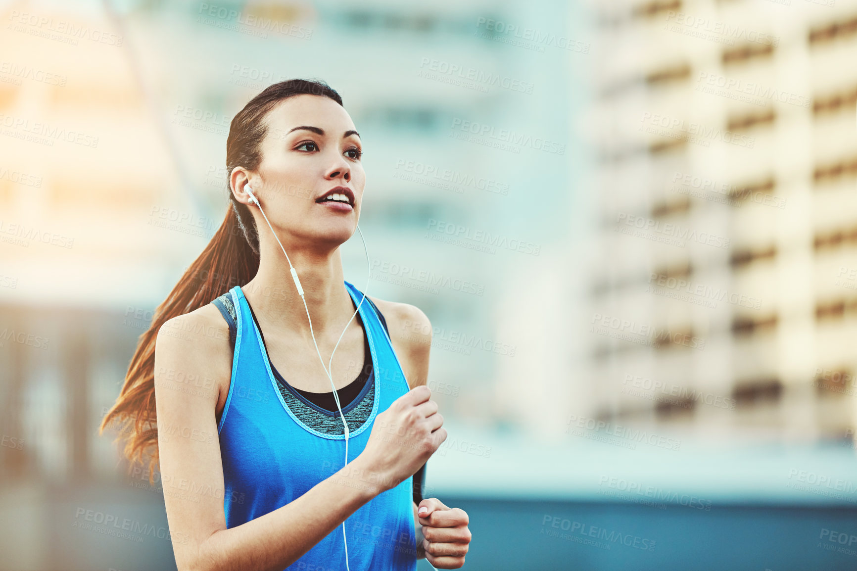 Buy stock photo Woman, earphones and running in city, morning and training for exercise, health and speed in street. Girl, person and runner with fitness, workout and audio streaming subscription by metro buildings