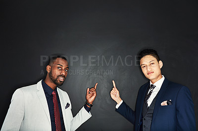 Buy stock photo Portrait of two young businessmen pointing against a dark background