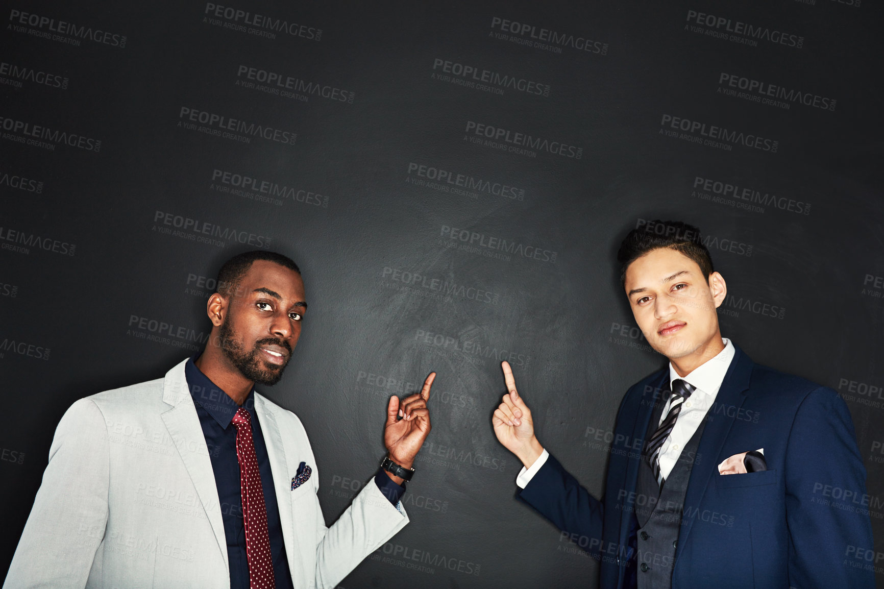 Buy stock photo Portrait of two young businessmen pointing against a dark background
