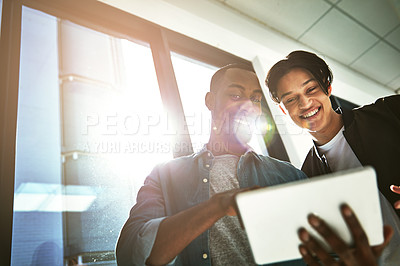 Buy stock photo Shot of two young colleagues looking at a tablet together in the office