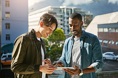 Buy stock photo Shot of two young colleagues looking at a tablet together while standing on a balcony outside their office
