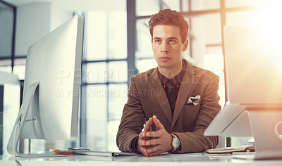 Buy stock photo Shot of a thoughtful young businessman working at his desk in a modern office