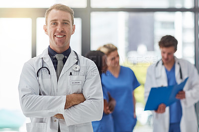 Buy stock photo Portrait of a young male doctor standing in a hospital with his colleagues in the background